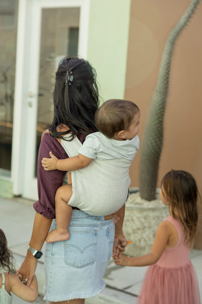 Mother carrying baby on back in natural Mamatoto Nomad baby carrier while walking with kids — practical ergonomic carrier for Australian mums.