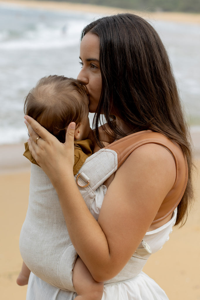 Mother kissing baby in Mamatoto Nest baby carrier at the beach — best baby carrier Australia for newborn bonding.