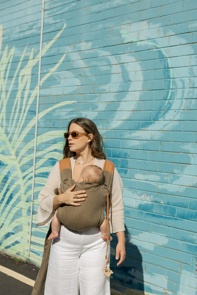 Smiling mother carrying newborn in olive Mamatoto Nest baby carrier — best newborn baby carrier in Australia.