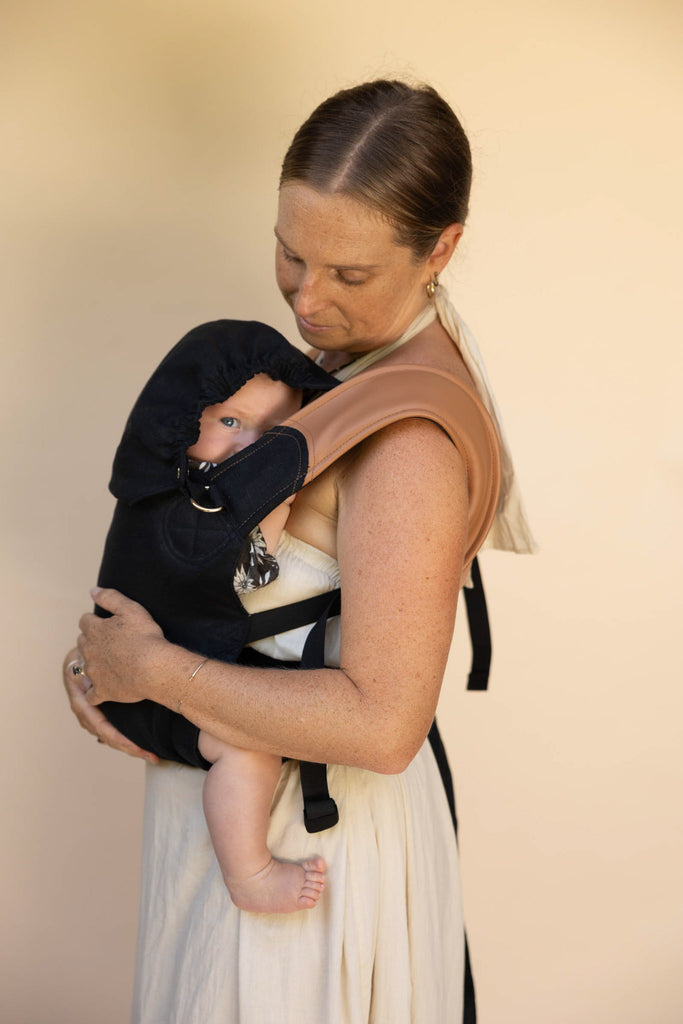 Baby protected in black Mamatoto Nest baby carrier with hood — ergonomic newborn carrier for Australian parents.