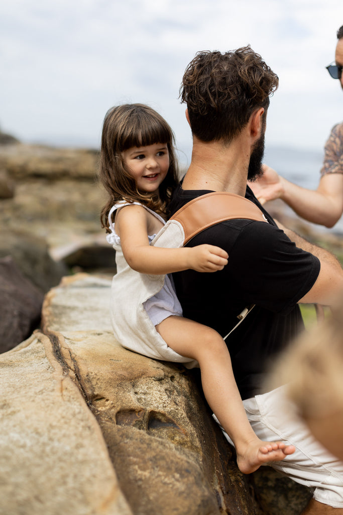 Dad putting toddler into Mamatoto Nomad ergonomic baby carrier — easy to use, hip-healthy design for parents.